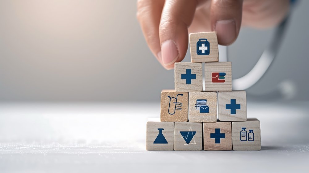 Hand setzt Holzbausteine mit Gesundheits- und Pflegesymbolen zu einer Pyramide zusammen – Symbol für Reformen und Aufbau im Pflegesystem.