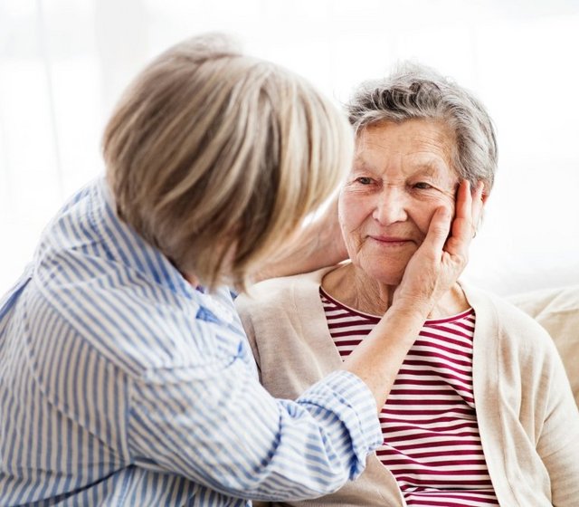 Tochter im Gespräch mit ihrer älteren Mutter im Wohnzimmer